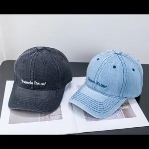 Detail of washed denim baseball caps in dark grey and light blue with Pamela Raina embroidery