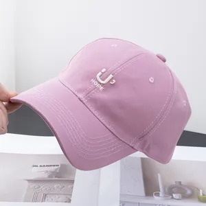 Detailed embroidery of letter U and smiley face on pink cotton baseball cap with white stitching