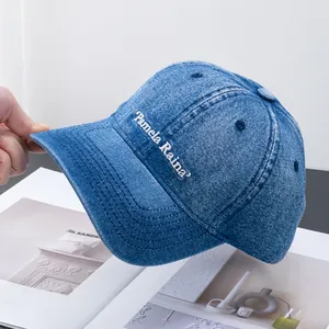 Detail of blue denim baseball cap featuring white Pamela Raina embroidery on the side