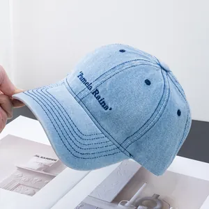 Detail of light blue denim baseball cap with navy Pamela Raina embroidery stitching