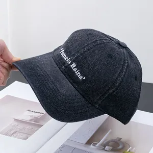 Detailed view of dark denim baseball cap featuring white Pamela Raina embroidery on the side