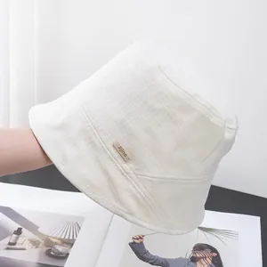 Detail of white textured cotton bucket hat with a small brown woven brand label