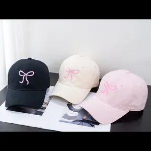 Three embroidered bow baseball caps in black beige and pink on a magazine background