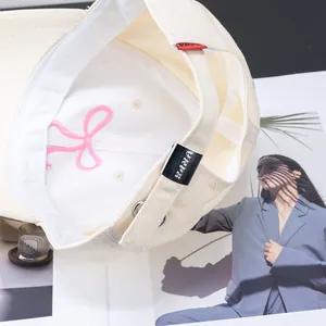 Beige cotton baseball cap with embroidered pink bow and adjustable silver buckle