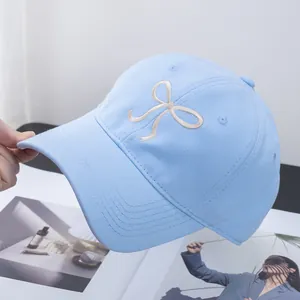 Detailed close-up of light blue baseball cap with white ribbon bow embroidery and stitching