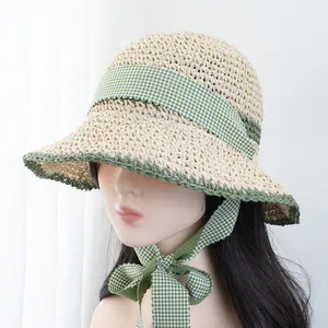 Detail of hand-woven straw hat featuring green plaid ribbon bow and contrast hem edging