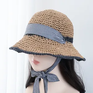 Detail of hand-woven straw hat featuring black wavy edges and plaid ribbon ties