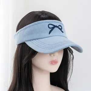 Detail of embroidered navy bow on light blue denim open top visor hat with curved stitching