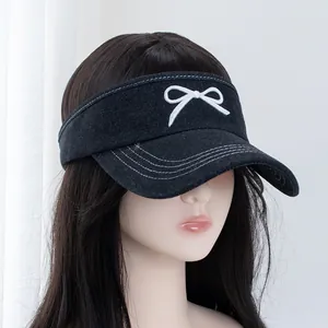 Detail of embroidered white bow and triple contrast stitching on black denim sun visor hat