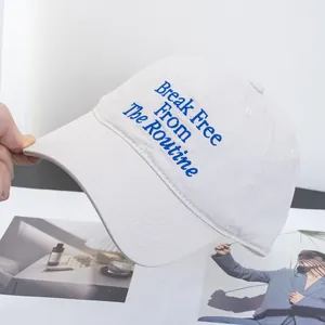 Detail of embroidered 'Break Free From The Routine' text on a cream baseball cap