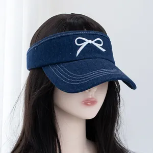 Close-up of navy denim sun visor hat with white embroidered bow and stitched brim