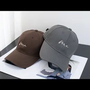 Detailed embroidery of white me script on brown and grey cotton twill baseball caps