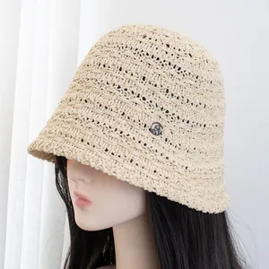 Dettaglio della trama del cappello a secchiello beige all'uncinetto con logo in metallo