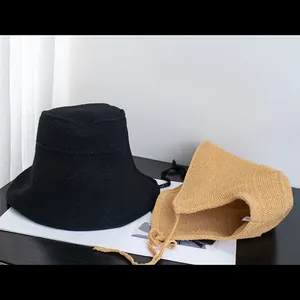 Detail of hand-woven cotton straw bucket hats in black and light brown with adjustable straps