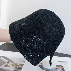 Dettaglio cappello da sole nero all'uncinetto con logo in metallo e trama intrecciata