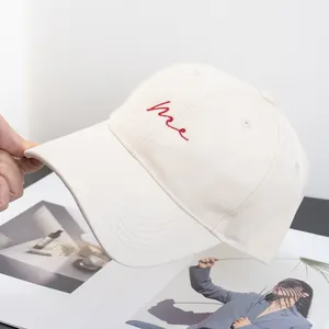 Detail of red me embroidery on a cream cotton twill baseball cap with curved brim