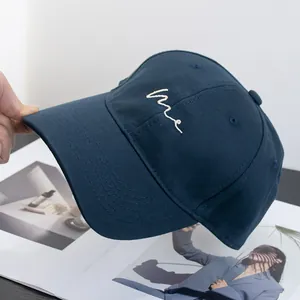 Detailed view of white 'me' embroidery on navy blue cotton baseball cap with curved brim