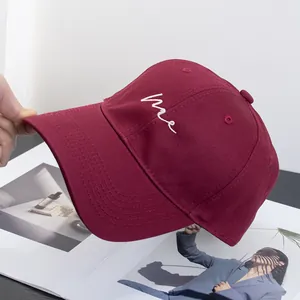Close-up of wine red cotton baseball cap with white cursive me embroidery and curved brim