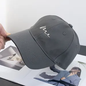 Detailed view of hand-held dark grey baseball cap with minimalist white me embroidery