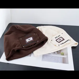 Dettaglio di berretti in maglia marrone e crema con toppe in tessuto vintage EST.1997