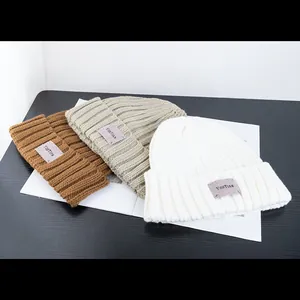 Detailed close-up of chunky knit beanies in white, khaki, and brown with woven labels