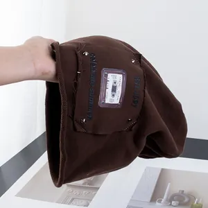 Dettaglio del berretto in maglia marrone caffè con patch vintage e rivetti argentati