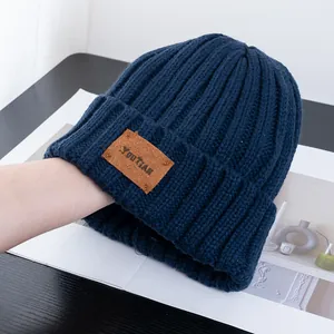 Macro detail of navy blue ribbed knit beanie with brown leather logo patch