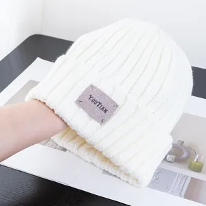 Close-up of white ribbed knit beanie featuring a grey rectangular YOUTIAN woven label