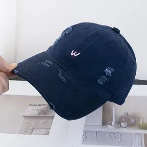 Détail macro d'une casquette vintage bleu marine avec broderie W rose et bords usés
