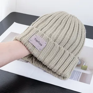 Detail of khaki ribbed knit beanie featuring a purple YOUTIAN woven patch on the fold