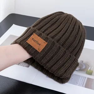 Detailed texture of dark brown ribbed knit beanie featuring a vintage leather logo patch