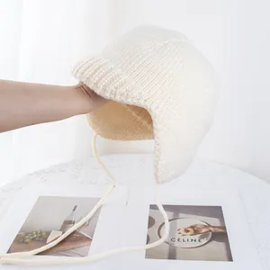 Detail der cremeweißen Strickmütze mit warmen Ohrenklappen und Bindebändern in der Hand