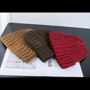 Dettaglio di berretti in maglia spessa nei colori cammello, marrone e bordeaux