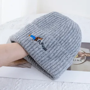 Gros plan sur un bonnet gris en maille avec broderie de teckel et lettrage détaillé