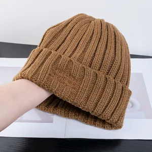 Dettaglio del berretto in maglia a coste marrone con ricamo tono su tono