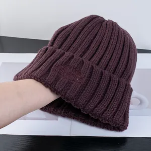 Dettaglio del berretto in maglia viola scuro con trama a coste e ricamo in tinta