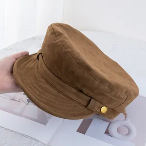 Detailed view of a brown suede baker boy hat with decorative band and gold button