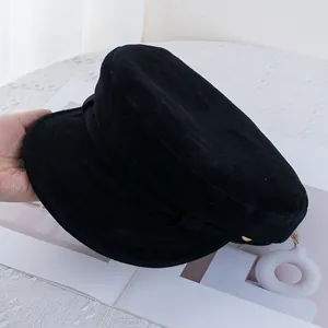 Close-up of black suede newsboy cap featuring a decorative gold button and flat top