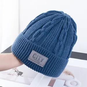 Detail van donkerblauwe gebreide muts met leren patch en dikke kabeltextuur