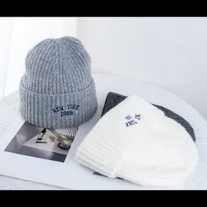 Three colors of wool knit beanies with New York embroidery on white textured background