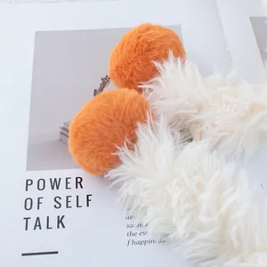 Détail de la texture en fausse fourrure avec pompons orange sur un bonnet d'hiver blanc