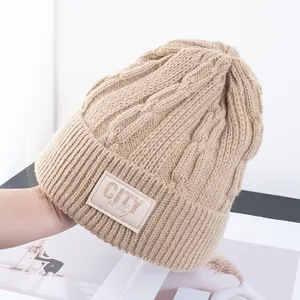 Detail van een camelkleurige gebreide muts met 'CITY' stoffen label en ribstructuur