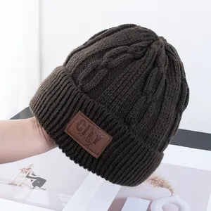 Detailopname van de dikke kabelgebreide textuur en het bruine leren label op de wintermuts