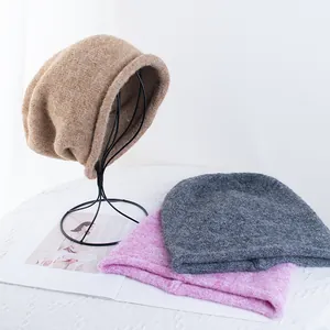 Primo piano di berretti in maglia morbida in kaki, grigio e rosa su supporto minimal