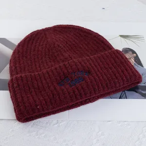 Close-up of burgundy knit wool beanie featuring blue NEW YORK 1986 letter embroidery