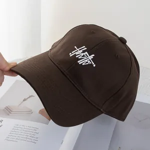Detail of dark brown cotton baseball cap featuring white artistic letter embroidery
