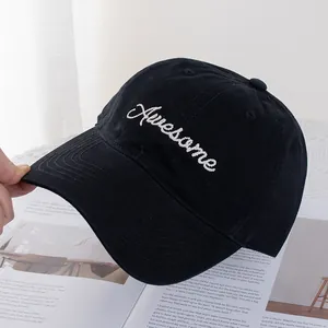 Detail of white Awesome embroidery on a black cotton baseball cap over a magazine