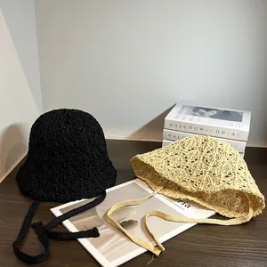 Dettaglio ravvicinato di cappelli a secchiello in paglia traforata con nastri nero e beige
