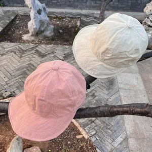 Lightweight quick-dry nylon baseball caps in pink and beige hanging on a branch outdoors
