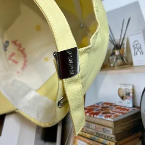 Dettaglio cappellino da baseball giallo chiaro con fibbia in metallo e scritte impresse